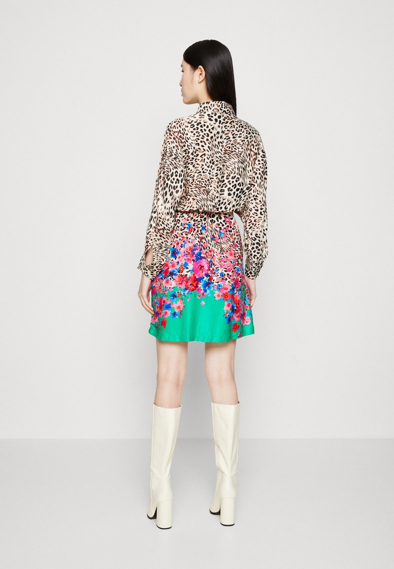 Blouse à motifs léopard avec des manches longues, taille cintrée, jupe à motifs floraux turquoise, accompagnée de bottes blanches jusqu'aux genoux.