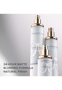 Drie cilindrische sprayflessen met een matte witte afwerking en gouden accenten. De etiketten zijn voorzien van de tekst "Impeccable Setting Spray" met productdetails eronder.