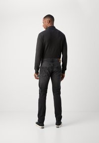 Sweater noir avec un col montant associé à un jean gris foncé. Le jean possède des poches arrières et une pièce en cuir beige sur la ceinture.