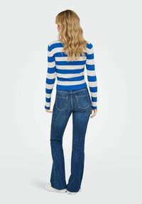 Pull rayé côtelé bleu et blanc associé à un jean foncé évasé. La tenue présente des manches longues et une silhouette ajustée.