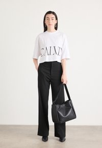 White cropped t-shirt with "CALVIN" in black letters, paired with wide black trousers. Black leather shoulder bag with matte texture.