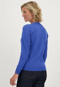 Blauwe gebreide trui met lange mouwen en een ronde hals. Heeft ribgebreide manchetten en zoom. Gecombineerd met donkere spijkerbroek.