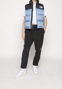 Kamizelka puchowa w jasno niebieskim i czarnym kolorze, zapinana na zamek, noszona na białej koszuli i czarnych spodniach, w połączeniu z białymi trampkami.