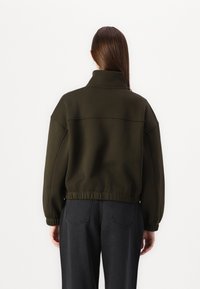 Olive green cropped jacket with a high collar, elastic waistband, and long sleeves. Smooth texture and minimalist design details.
