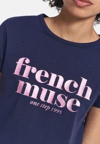 Camiseta azul marino hecha de algodón suave; presenta un texto brillante en rosa que dice "musa francesa" y "un paso 1995" en una fuente gruesa. Cuello redondo.