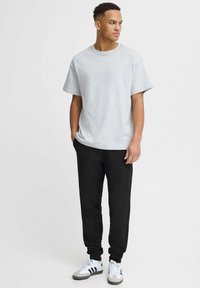 Grå bomull T-skjorte med korte ermer kombinert med svarte joggebukser. Modellen står i en nøytral posisjon. Hvit og svart joggesko fullfører antrekket.