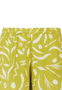 Pantaloni verde lime con un motivo astratto bianco. Presentano una fascia elastica in vita e un tessuto morbido e testurizzato. Il design include vortici e cerchi.