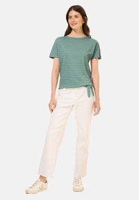 Tyrkysový pruhovaný top s krátkým rukávem a uzlem na boku, spárovaný s bílými širokými kalhotami a béžovými teniskami.