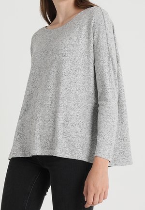 Maglia grigia a maniche lunghe con collo rotondo e vestibilità leggermente ampia. Tessuto testurizzato con un motivo melange, abbinata a jeans scuri.