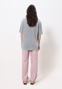 Helles graues, übergroßes T-Shirt aus weichem Stoff, kombiniert mit locker sitzenden, hellrosa Hosen mit verblasster Textur und umgeschlagenen Säumen.