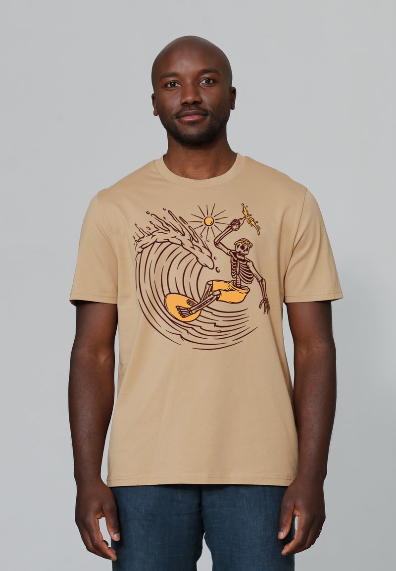 Beige t-shirt met een graphic van een skelet dat surft op een golf, met donkerbruine omlijning en een oranje zon op de achtergrond.
