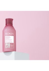Après-shampooing Redken Volume Injection dans une bouteille en plastique rose à la forme arrondie. Dispose d'un couvercle à rabat et d'un texte blanc sur l'étiquette.