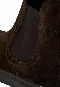 Bottine en daim marron avec panneaux latéraux élastiques et coutures décoratives. Tige texturée et semelle en caoutchouc pour la durabilité et l'adhérence.