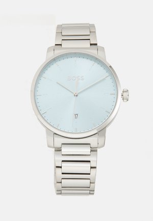 Reloj de pulsera plateado con un dial azul claro, correa de acero inoxidable, diseño minimalista y función de fecha en la posición de las 6 en punto.