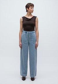 Καφέ αμάνικη μπλούζα με στρογγυλή λαιμόκοψη, συνδυασμένη με ψηλόμεσα ανοιχτό μπλε τζιν παντελόνια με ελαστική μέση και κορδόνι.