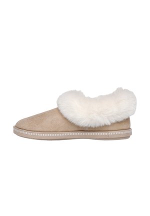 Mocassin en suède beige avec col en fausse fourrure blanche, semelle plate, bout arrondi et couture décorative le long de la semelle. Texture douce et design confortable.