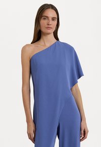 Asymmetrisk one-shoulder jumpsuit i lyseblå stof med en glat overflade; har en draperet ærme og en tætsiddende silhuet.