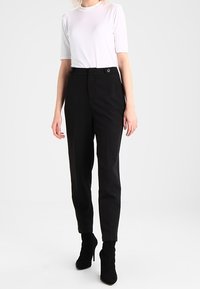 Pantalons noirs ajustés à taille haute, avec des poches avant et une fermeture à bouton, associés à un haut blanc ajusté à manches courtes.