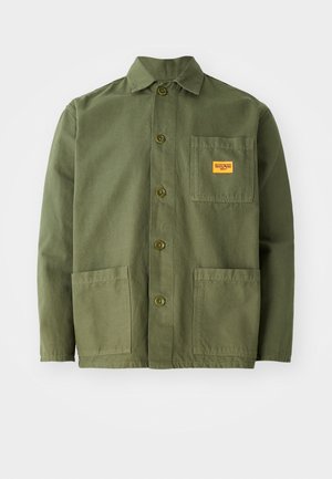 Olivgrüne Jacke aus schwerem Baumwollmaterial, mit spitzem Kragen, Knöpfen auf der Vorderseite und zwei großen aufgesetzten Taschen. Mit einem kleinen Logo-Patch versehen.