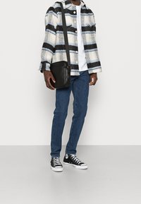 Camicia di flanella a quadri neri, blu e bianchi; t-shirt bianca; jeans in denim blu; borsa a tracolla in pelle nera; sneakers alte bianche e nere.