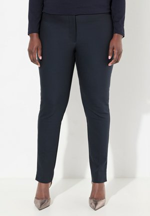 Marineblaue Slim-Fit-Hosen mit glatter Textur, dezentem Vordernaht und elastischem Bund; kombiniert mit metallischen spitzen Absätzen.