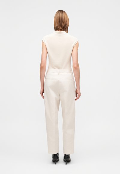 Tiimalasimallinen kerma-toppi, jossa on lyhyet hihat, yhdistettynä vaaleanbeigeihin korkeavyötäröisiin housuihin, molemmat sileäpintaisia. Mustat korkokengät.