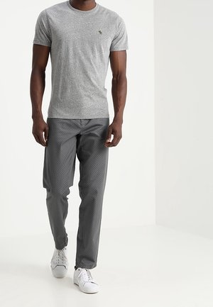Szary t-shirt z krótkim rękawem, okrągłym dekoltem i małym logo, połączony z szarymi spodniami w wzory oraz białymi sneakersami.
