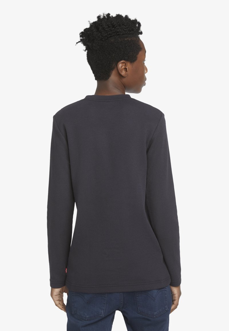 Maglietta a maniche lunghe in tessuto waffle di un blu navy scuro, con scollatura rotonda e un piccolo logo sul bordo sinistro inferiore.