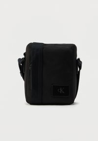 Μαύρη υφασμάτινη τσάντα χιαστί με ορθογώνιο σχήμα, που διαθέτει λεία υφή, μπροστινό λάβαρο με λογότυπο και ρυθμιζόμενο ιμάντα.