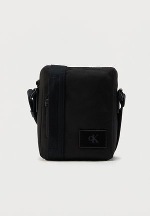 Melnas auduma plecu soma ar taisnstūrveida formu, gludu tekstūru, priekšpusē logotipa uzlika un regulējamu siksnu.