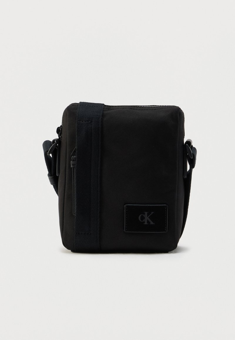 Μαύρη υφασμάτινη τσάντα χιαστί με ορθογώνιο σχήμα, που διαθέτει λεία υφή, μπροστινό λάβαρο με λογότυπο και ρυθμιζόμενο ιμάντα.