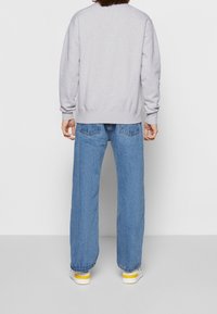 Felpa grigia con maniche lunghe, polsini e vita a costine, abbinata a jeans a gamba larga e scarpe con accenti gialli.