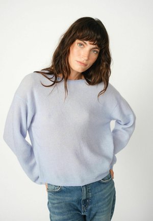 Pull bleu clair en maille douce avec une coupe décontractée, des épaules tombantes et un col rond, associé à un jean en denim.