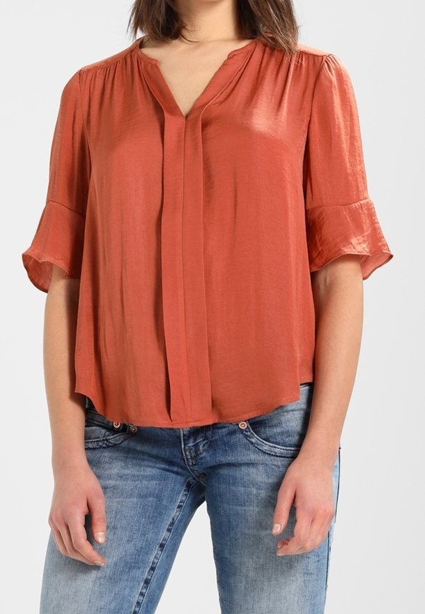 Blouse à manches courtes couleur rouille avec encolure en V, coupe ample et détails de plis délicats aux épaules. Tissu doux et lisse.