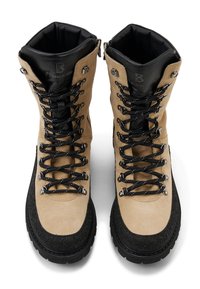 Světle hnědé turistické boty z broušené kůže s černými gumovými podrážkami, černými tkaničkami, kovovými očky a polstrovanou vnitřní výstelkou.