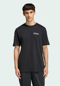 Black cotton T-shirt with short sleeves and crew neck. Features white "Adidas" logo on the left chest. Simple, classic design.
