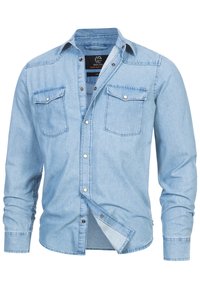 Light blue denim shirt with long sleeves, two chest pockets, and button-down front. Features white stitching and black logo on the collar.