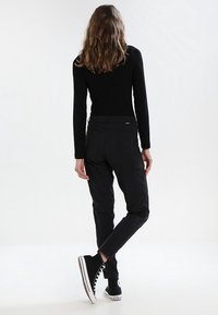 Černé přiléhavé kalhoty s hladkou texturou, vybavené kapsami a kónickými nohavicemi. Nosit je s černým dlouhým rukávem a černými teniskami.