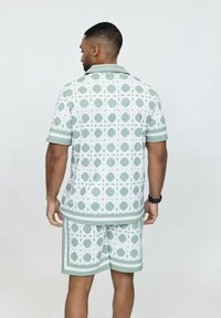 Ensemble chemise à manches courtes et short en vert clair avec un motif géométrique blanc, comprenant un col et des rayures contrastantes sur les manches.