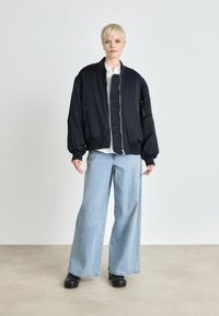 Navy bomber jacket with a quilted front, ribbed cuffs, and base; paired with light blue wide-leg jeans and black platform shoes.