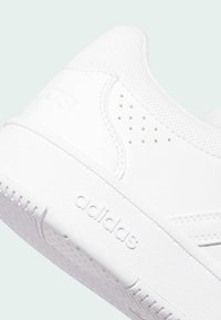 Biele športové topánky s hladkým syntetickým zvrškom, textúrovanou sieťovinovou panely, perforovanými akcentmi a gumovou podrážkou s logom.