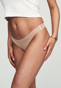 Nude Slips aus glattem Material, mit nahtlosem Design, dünnen Trägern und einem dezenten Logo am Bund.