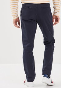 Marinblå bomullsbyxor med slim fit, som har två bakfickor och en subtil struktur, parat med vita sneakers med blåa och röda detaljer.
