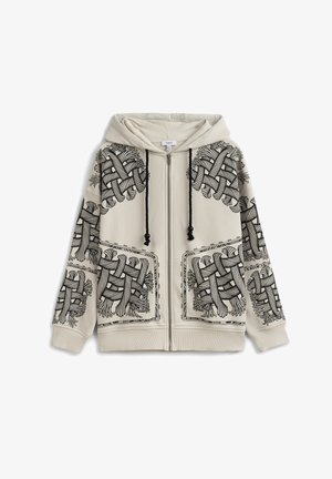 Beige hoodie met ritssluiting, voorzien van zwarte abstracte geweven touwontwerpen op de schouders, voorzakken, mouwen en zwarte trekkoorden aan de capuchon.