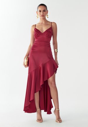 Czerwona satynowa sukienka z dopasowaną górą o dekolcie w kształcie litery V, regulowanymi ramiączkami, asymetrycznym dołem i falbanami. W zestawie złote dodatki.