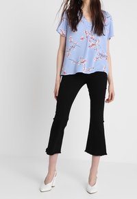 Blusa azul claro de manga corta y estampado floral; combinada con pantalones cortos negros y zapatos de tacón bloque blanco.