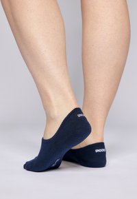 Calzini alla caviglia blu navy realizzati in tessuto morbido, con un design minimale e logo sul tallone. Pelle visibile e gambe con texture sullo sfondo.
