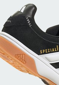 Svart mocka- och lädersneakers med vita accenter, texturerad gummisula och guld "SPEZIAL" logotyp nära hälen.