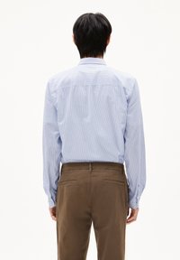 Blauw-witte gestreepte blouse met lange mouwen en knoopmanchetten, gedragen met een paar bruine broeken. De blouse heeft een standaard kraag en een rechte snit.