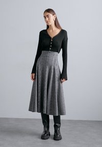 Črn rebrast dolg rokav s gumbasto patento, v kombinaciji z dolgo karirasto krilo v črno-beli barvi, nošeno s črnimi čevlji do kolen.